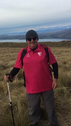 Image of a man standing with a hiking stick with mountains and lake background